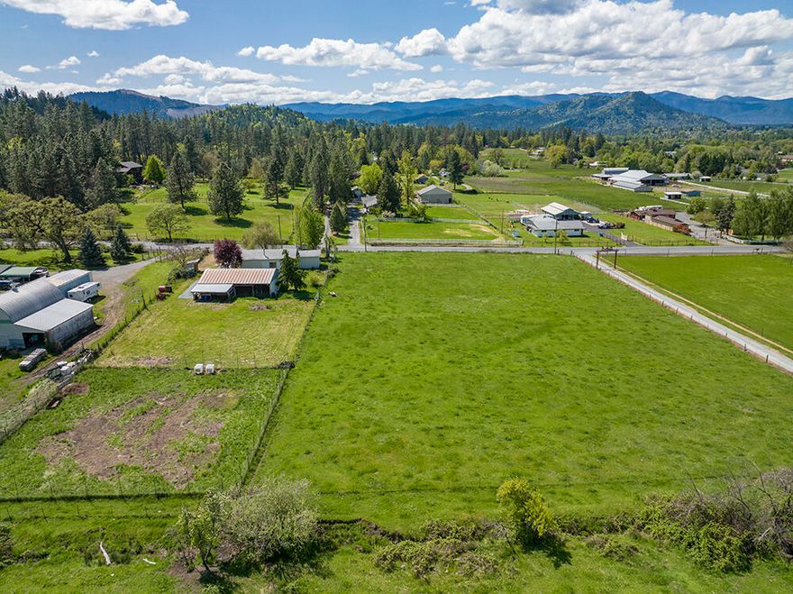 Rare Jerome Prairie Acreage w/ Improvements; 5.03 acres w/ well, septic, barn & large RV garage w/ office & one of the only unobstructed westward mountain views in Jerome Prairie (you'll love the sunsets!). Fenced, cross-fenced & gated w/ circular drive & new culverts at the entrances. Established landscape, fruit trees & a peaceful country setting w/ a Willow tree out front. Dry barn, dog kennel, chicken coop, above ground 300-gallon fuel storage, fenced garden area. Water flows from a neighboring pond through a drainage ditch, forming a small seasonal creek between pastures. 5 -10 min to downtown Grants Pass in a desirable area of horse country w/ riding trails on Bolt Mtn nearby. New Roof being installed on the RV Garage thru 5/22 –  Showing by Appt only.