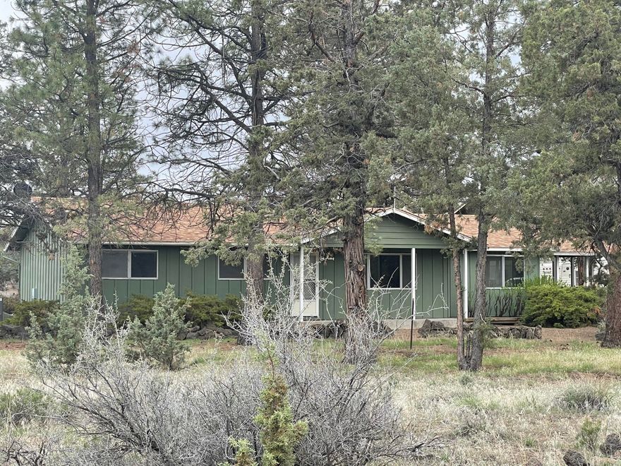 Looking for a little country living with lots of privacy? This three bedroom two bath ranch style home on rural property close to Bend offers that and much more at an affordable price.  The lay out includes a living Room, Kitchen, Utility and Family Room.  It also has a detached double car garage with single car garage door.  Above the garage is possible additional living quarters, which Includes a decommissioned kitchen, along with a full bath and closet, it needs some TLC.  Outbuilding are a small barn/loafing shed and a playhouse. The home has a large covered porch area off to the side of the home. It has been newly carpeted, with a newer roof and 1000 gallon concrete septic tank.