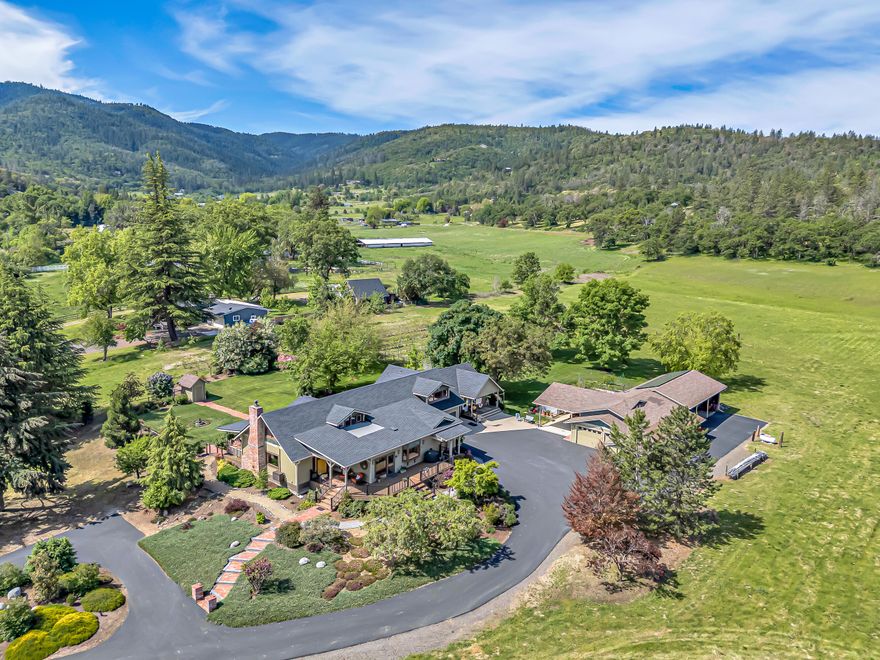 Paradise in Southern Oregon exists alongside Griffin Creek at this unique setting on over 10 luscious acres. Cross the gated moat and experience a 4,044 sq. ft. 3-bed, 3.5 bath home boasting quality construction, knotty alder trim thru-out and great living areas. The open beam great room features a lovely rock fireplace and stunning views across the immaculate grounds. In the chef's kitchen is a huge island with 5-burner cooktop, granite & marble counters, and more stunning vistas. Main floor primary bedroom is very spacious with a very distinctive bathroom set-up featuring his and hers bathrooms & shared walk-in shower. There is a complete 1-bedroom guest cottage with amazing views; a detached garage with attached shop and carports areas; a large equipment shed, over a ¼ acre of blueberries and plenty of fenced yards for dogs, kids and entertaining. The land is fully irrigated and has large, raised garden beds. This lovely home and property is more than just a home - it's a lifestyle