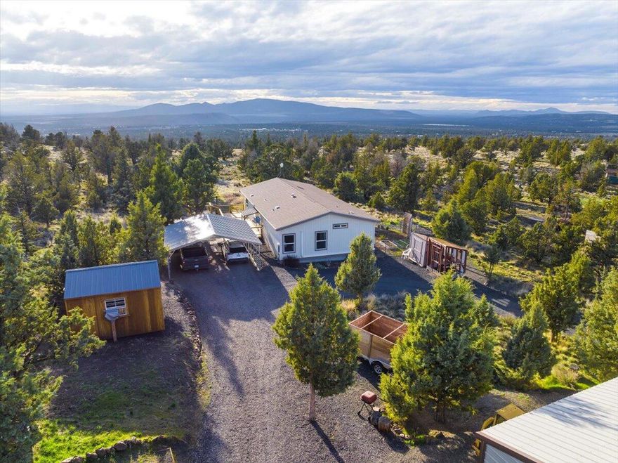 Offering $5,000 seller closing credit to buyers! Bring all your toys to this spacious oasis at the top of the hill in Prineville Lake Acres 1! Adjacent to thousands of acres of BLM land, ride your ATV to the reservoir! Panoramic views of the cascades greet you from the back deck. Featuring a fully fenced 1.84 acres and 6 outbuildings for workshops, potential guests' quarters, or your fitness studio! 600 sq ft shop with power and a woodstove. A circle driveway with 2 gates allows easy access. Built in 2017, this home feels brand-new! Sellers have added cedar decking to take advantage of the stellar views, a water softening system, and a Mini-split for heating and cooling (in addition to central heat!). An abundance of natural light, recessed ceilings, a massive primary bathroom and walk-in closet, and an open concept floor plan are just a few highlights. If you have been looking for extra space and breathtaking views, this one's for you!