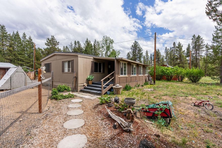 Charming and clean Mobile home on a serene tastefully developed half-acre. Tucked away from the hustle and bustle, this peaceful property is a springboard into endless outdoor adventures. The interior of the main home is well-loved with thoughtful improvements for comfortable living. Enjoy your morning coffee while viewing the wildlife from the covered front porch. The exterior is more than just beautifully landscaped with Garden, Gazebo, and Greenhouse; it boasts functionality with multiple sheds, RV storage and RV hook up behind a fenced and gated entry. The detached guest house includes a kitchen, bathroom, bedroom, and workshop; complete with its own breaker box and 220amp power, ideal for projects, creative work and hobbies. The guest house electricity and water are unpermitted but come from the same supply that nourishes the main home. This property blends comfort, charm and versatility.