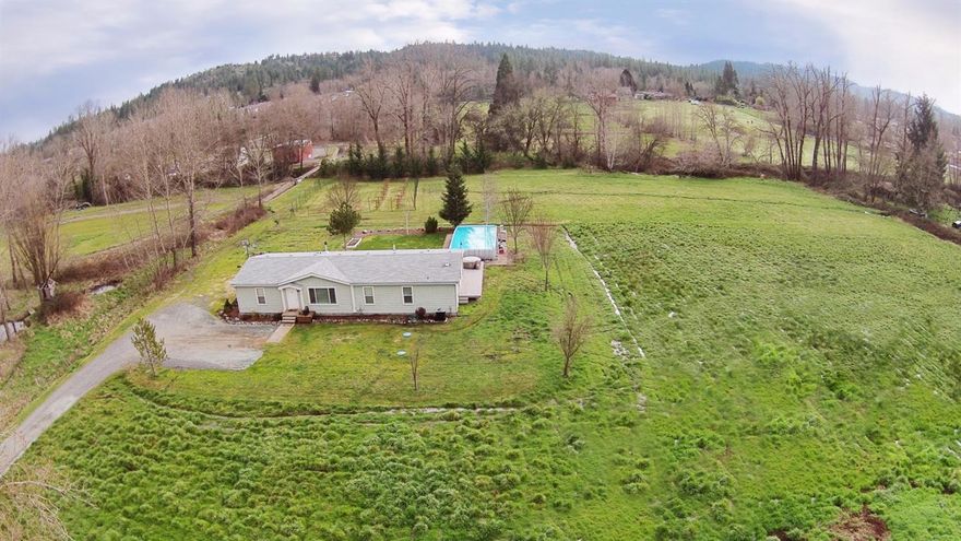 Minutes from town, rests a well cared for 2005 Manufactured home on 4.67 irr.acres. This 3bdrm, 2bth home has recently been updated with new flooring, fresh paint, & has an open floor plan. Ample storage throughout the home, laundry room, & hallway. Guest bdrms measure just under 15'X10'. Home has a large mstr bdrm w/ walk in closet, and separate seating area that could be used as a mini office or reading area. Wood stove provides an area to sit and relax, as well as adding additional warmth during the cool winter eves. As you enter the long driveway, you pass by the recently painted 40'X90'indoor arena, with 7 stalls, and a tack room. There is an accessory building that can be used for storage, or a future hardship dwelling. The home sits well off the road, on very useable acreage, and has a legal 25X60 RV Pad permitted with the County. At the rear of the home is just under 500 sq ft of decking, that overlooks a pasture, small orchard, Allen Creek, and the above ground saltwater pool.