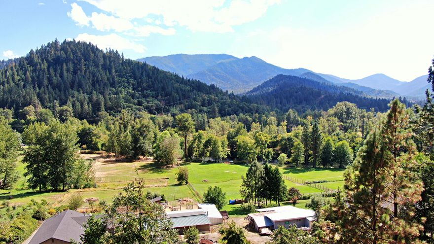 Here is a well-maintained home on N Applegate Rd with majestic valley views & views of the Applegate River. There is a massive 1500 sq/ft back deck for enjoying the outdoor serenity.  Home has 3 bedrooms, 2 bathrooms, laundry room plus great pantry storage, open kitchen with bar counter, open front door entry room with vaulted tongue & groove ceiling, useful covered breezeway between the home & the garage, the garage has lots of built-in storage with doors that close, a detached 450 sq/ft building that could be used as a hobby/game room or a potential ADU, full RV hookups with 50amp power. The home offers a gated entry with a full wrap around paved driveway, chain-link fencing, 28x20 covered carport with additional attached covered work area & loft, with another covered boat/trailer building, & a covered area that was once used as a horse stall area with arena. Per the Seller the well is 20+ gpm, plus irrigation rights.