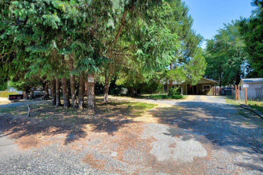 Seller offering 3k buyer credit at closing upon request. This charming three-bedroom, 1.5-bathroom home is situated on a spacious lot with a wooded front, providing a sense of privacy and tranquility. Located by Fruitdale Elementary, the property spans just under a half acre with Grants Pass Irrigation. The home features its own well with a new pump, ensuring reliable water access, and a new gutter system to improve drainage. The large, fenced backyard includes a storage shed or shop to match the front one. One shed has a fenced area ideal for a garden, while the other is perfect for animals or small dogs. This property offer a unique blend of convenience and seclusion in  town.