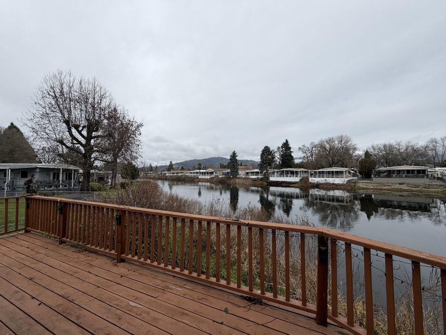 Cute and comfortable manufactured home on the lake in Rogue Lea Estates. Enjoy watching birds and other wildlife from the large living-room windows or from the deck overlooking the water. This 2-bedroom, 2-bath 1100 sq ft home was updated 3 ½ years ago. It features refreshed kitchen with nice appliances, including a gas cooktop and pantry. Primary suite has a walk in closet and additional closet space. Natural gas heat and water heater. Single-car carport with additional storage. Lease space is $1070 per month and $31.00 for sewer and trash. Water is shared wells.