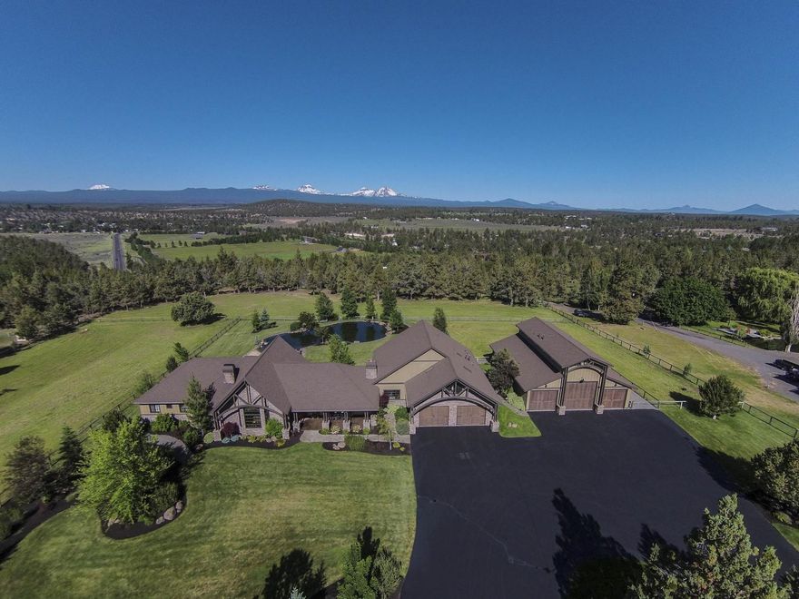 This 4593 SF 2 story farmhouse lodge uses cultured stone & natural finishes, blending it into the scenic landscape of Tumalo while quietly overlooking the Cascades & its own swimming pond. The NW Style is emphasized w/ Lg windows facing the views & exposed framing. Separate, heated 3 Bay shop w/ apt. offers space to hook up a 45' RV & stow a bevy of boats, ATVs, etc. Open floorplan custom designed to capture mtn views from nearly every room. Unique details like reclaimed hardwood floors & beams. Mostly main level living w/ ample Bonus Rm & Powder up. Kitchen & dining offer space to seat 14 & a cozy bay window & 2nd FP. The Thermador dbl ovens & 48'' six burner range w/griddle pair nicely w/ Lg farmhouse sink & granite counters. Primary bd overlooks Cascades & pond. Accordion glass doors lead to expansive patio & hot tub. 5 lush, irrigated acres offer the experience of farm living close to town. Such a halcyon estate is not only a privilege to visit, but also a rare opportunity to own.