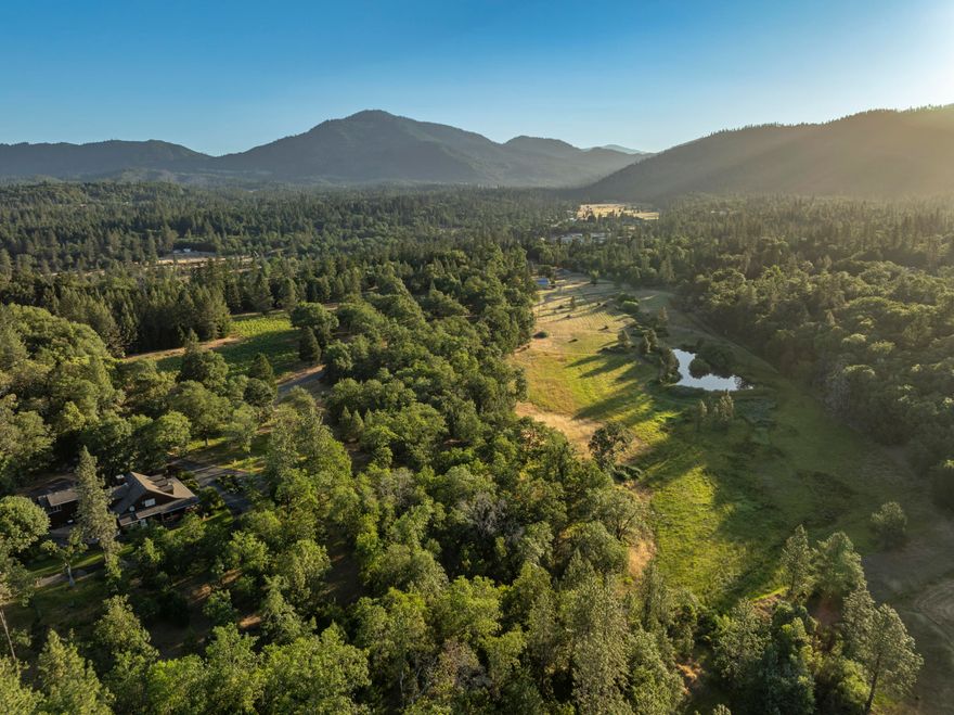 Tucked into a private valley just minutes from Grants Pass, this 37.76-acre estate blends natural beauty, privacy, & rural living. Behind a gated entrance, the land features rolling pasture, mature timber, a boutique vineyard, & a peaceful setting few know exists. The custom home sits on a knoll among oaks and pines, with main-level living, guest rooms upstairs, & a bonus room over the garage. Elegant design elements, including rich wood trim, built-ins, & a spacious kitchen with two pantries. Enjoy outdoor living with expansive decks, mature landscaping, & a whole-house generator. The large 2,240 sq ft shop offers space for equipment, hobbies, or creative projects. Additional improvements include a greenhouse, garden, carport, & chip-sealed drive. A permitted irrigation well supports both household & irrigation needs, while a ½ acre pond adds charm and wildlife habitat. Ideal for a hobby farm, small horse ranch or homesteading paradise, this is rural Oregon living at its best.