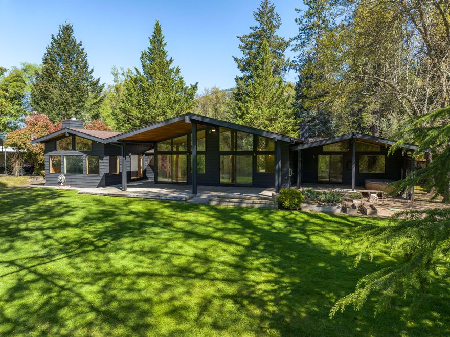 Exceptional Southern Oregon riverfront retreat on 6.12 private acres with direct Rogue River access. This architecturally distinct mid-century modern home offers 3,589 sq ft of single-level living with vaulted ceilings, wall-to-wall windows, and a chef's kitchen designed for entertaining. Step outside to an expansive patio with sweeping river views, a private beach, and lush lawn leading to one of the river's premier fishing holes. The property also features a guest house, multiple garages, workshops, RV hookups, and seasonal ponds. Zoned RR1 with separate utilities and septic systems, this estate offers compelling potential for future subdivision, multigenerational living, or income production. Located just 10 minutes to downtown Grants Pass—rare riverfront opportunities like this are limited and in demand. Schedule your private tour today.