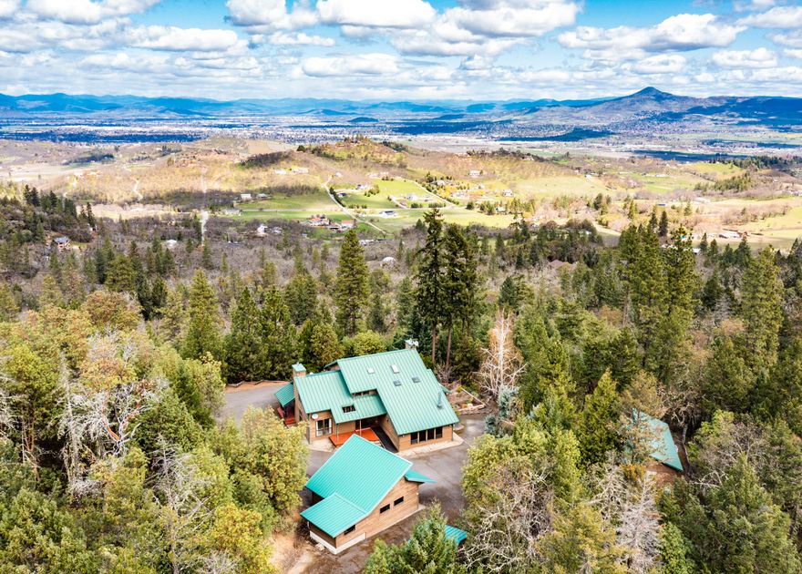 Dynamic country home with stunning panoramic valley views on secluded acreage with two separate detached garage/shop/office outbuildings -- all only 10 minutes from town! Home features cedar siding, metal roof, covered wrap-around porch, soaring vaulted ceilings, abundant natural light from multiple skylights and large double-paned vinyl windows, Hunter Douglas blinds, sunroom, gas fireplace with travertine stone hearth, formal and informal dining areas, gorgeous solid maple floors, along with a spacious bonus room with knotty pine paneling. Kitchen equipped with leathered granite counters, island, four-burner electric range, freestanding gas stove, and pantry. Main level full bath and office; upper level with three generous bedrooms and two full baths including en-suite master with private balcony, marble tile, jetted tub, and expansive walk-in closet. Sunny deer-resistant gardens and mature landscaping. Inquire with agents for details on well, water purity, and high-speed internet.