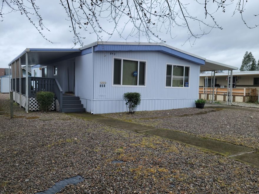 Nice sized doublewide mobile home with minimal lawn care, two sheds AND access thru an alley. In the Primary Bedroom's en-suite bathroom, is a custom tiled walk-in shower with grab bars and a seat. The second bedroom also has an attached bathroom with grab bars and a walk thru to the laundry room. The kitchen sports a breakfast bar, a pantry and electric appliances. Enjoy the outside while sitting under your covered deck that spans the side of the home from the living-room to a slider in the dining room.  This home is just minutes from the Rogue River. There is additional RV parking provided by the park for an additional fee. Clubhouse has occasional celebrations inside and outside! Rogue Lea Estates is located close to downtown Grants Pass for shopping and restaurants. Don't miss this one! Call now for an appointment. Call now for an appointment.