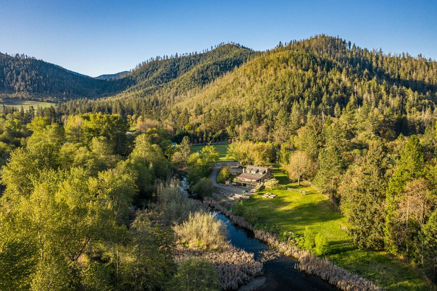 This is the quintessential family farm & outdoor lifestyle. The 11.49-acre property features a lovely home that overlooks a 3-acre pond, with live flow from the Applegate River. The grounds are simply beautiful with sprawling lawns, irrigated pasture, fantastic raised bed garden, fruit trees, berries, a tree lined entry & ample water. Custom built in 1982, the architectural style & lines of this home embody the charm & elegance of an early 20th century three-level farmhouse. Throughout the main living area, you will find hardwood floors, natural wood details & farmhouse style finishes. Outside is a large east facing covered deck that takes in the beautiful setting. Set up with permaculture in mind, the land has water rights for 4.4-acres, 5 acres of class-one loam soils, & an automated irrigation system. Improvements include a renovated barn set up to be a recreation center, shop, goat barn, chicken coop, garden shed, tiny'' cottage, play structure, walking trails & more!