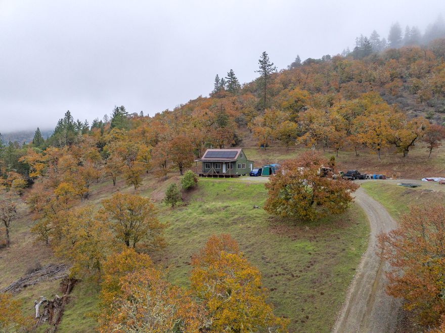 Perched on a quiet country road, this 5-acre Applegate Valley retreat borders over 200 acres of public land & showcases panoramic views across the valley below. The off-grid cabin is powered by a solar array with battery storage & offers a comfortable layout with a living room, kitchen, bath, laundry, & a large lofted bedroom. The covered front porch is the perfect spot to enjoy the sunset & take in the scenery. With both southern & western exposure, the property enjoys midday sunlight year-round - plus amazing sunsets! For those envisioning new construction, the terraced homesite includes a driveway & septic system already in place. Modern conveniences of Grants Pass are within a 30 minute drive - medical, groceries, banking, dining, & more. Whether you continue the off-grid lifestyle or build your dream home, this property captures the best of Southern Oregon living—privacy, views, & access to endless outdoor recreation in one of the most beautiful regions in the Pacific Northwest.