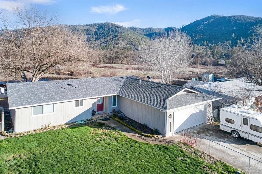 This charming home is surrounded by beautiful mountain views. Warm and cozy feel with wood laminate flooring and multi-pane French doors in the living room that look out on the beautiful backyard and surrounding view. The kitchen has a gas stove and tile counters with a large butcher block section of counter. Enjoy summer BBQs with the expansive deck, yard with mature landscaping and a covered patio area. There is even a place for a hot tub and room for an above ground pool. The roof is less than three years old and the home is well maintained. Plenty of storage in the oversized 2 car garage and there is room to park a small RV to the side of the driveway. The front and back yards are fully fenced and the neighborhood is very peaceful. Feels like country but just blocks from downtown Rogue River.