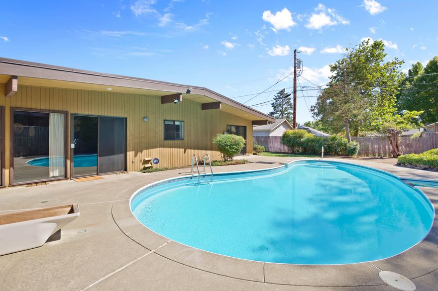 This Mid Century Modern home is a 3-bedroom, 2-bath nestled on nearly 1/3 acre! Located in a highly desirable NW Grants Pass neighborhood, complete with beautifully manicured grounds, mountain views, brand new TPO roof and a sparkling inground pool with spa. Mid-century enthusiasts will love the style and details, from the black-and-gold accents to the sunken living room featuring built-ins, a wood-burning fireplace, and dramatic floor-to-ceiling windows. The kitchen boasts stainless steel appliances and flows into a versatile space perfect for formal dining or a family room. Each bedroom includes sliding glass doors that open to it's own patio, creating seamless indoor-outdoor living. Two car carport with an additional shop area provides flexibility—ideal for hobbies, storage, or even a potential guest suite. With its unique character, open layout, and outdoor amenities, this home is a rare find. Come see all it has to offer!