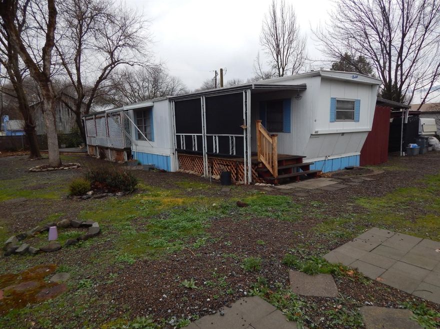 Wanting to get out of renting? Or searching for somewhere to build? Begin Here! It's a vintage 2/1 single-wide on almost a quarter acre lot where newer homes are popping up in the neighborhood. The comfortable home has laminate floors, a built-in hutch, gas heat & a tip-out for extra living room. The kitchen makes every square inch count. Cozy & efficient. A big deck under the tree in the backyard, a couple of storage sheds, a greenhouse, a vintage travel trailer for overnight guests, a screened-in side porch in addition to the front porch & a carport round out the outside. Along the back fence line you'll find 2 TID spigots for irrigation. Just hook up your hoses. There's also an extra storage area with a second fridge just outside the kitchen door. Big yard-Quiet street.