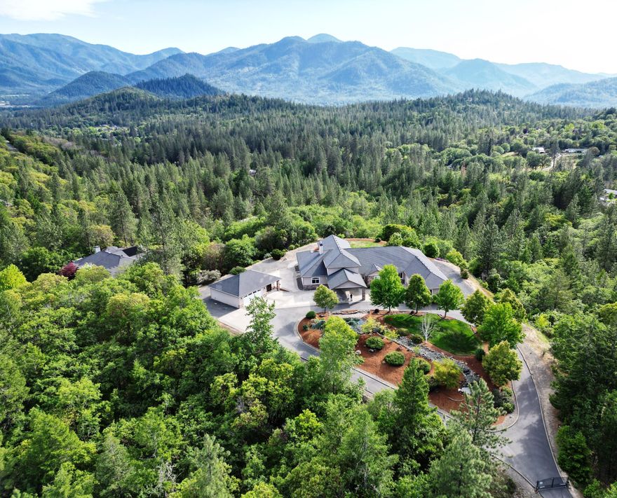 Southern Oregon Hilltop Estate nestled 4 miles from Grants Pass. This 5,062 sq. ft. estate offers exceptional luxury & versatility. The home boasts 4 en-suite bedrooms w/ a split floor plan for privacy. The grand entry room features 18' ceilings, fireplace, spiral staircase to loft/office & stunning bay windows/french doors to the covered lanai. A gourmet kitchen w/2 granite islands, 6-burner chef's cooktop & ample room for entertainment. Brazilian cherry floors run throughout the home, adding elegance. The theater room is ideal for movie nights, & the large lanai overlooks the mature irrigated landscape. State of the art ceiling speakers inside & out! The paved circular driveway with a porte cochere entrance showcases a 120' water feature with ponds, waterfall, lush lawn visible as you arrive through the gated entry. The property includes an oversized 2-car & a detached 2-car garage w/ full bath, guest quarters & mini split. RV hookups, backup generator, 18gpm well & more!