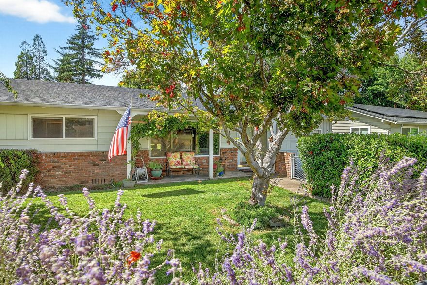 Welcome to this light filled ranch-style home beaming with charm and character. The inviting living room showcases a classic brick-framed wood-burning fireplace, creating a warm and welcoming focal point. The galley-style kitchen offers abundant cabinet space and a practical layout, conveniently located next to the dining room. The spacious primary suite features a private ensuite bath and slider access to the covered back patio. Two additional bedrooms are generously sized with an additional bathroom in the hallway. Outside, enjoy the expansive backyard with its park-like setting, covered patio, and additional storage sheds. This home combines comfort, functionality, and timeless appeal. The adjoining 0.19-acre tax lot is also available for purchase at $150,000, offering future opportunities and added flexibility.