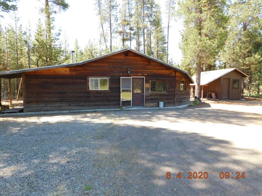 Looking for that perfect cabin in the woods? Here is a rustic style cabin w/ 3 bdrms & 1 bath w/ a formal dining that could also make a great office. There are 2 beams along the vaulted ceiling & no hallways, so this home feels quite large. Seller has updated all the flooring w/wood & 12-inch tiles. Newer cabinets w/new tiled countertops in kitchen & on bathroom cabinet, tile surrounding the shower/tub unit &  is fully plumbed for washer & dryer unit. This home really needs someone to love & finish it. A lot has been done, but not all the finish work. Is in a great rural neighborhood w/low traffic on an acre w/private septic & well. There is a slab already poured & ready for a new garage. The pumphouse has extra storage, a small shop area & a covered area off the side. The back door opens on to a concrete pad & covered firewood area. Circular driveway w/lots of room for a shop, barn or whatever your needs are. The back of property borders private forest land. Sold AS IS