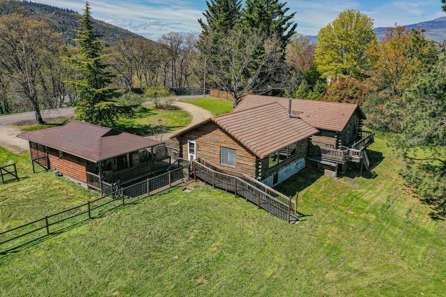 Stunning mountain and lake views from this log home with detached artist studio just 10 minutes to Ashland! Set on 3+ acres with deeded water rights, this single-level, 3-bedroom, 2-bathroom home features a welcoming foyer, vaulted living room log truss-beams, a wall of windows showcasing
Ashland's southeast hills, hardwood flooring, raised hearth woodstove, galley style kitchen and large connected dining space. The separate wing of bedrooms and bathrooms includes a convenient laundry area and access to a large view deck. The artist studio (288sf) with a full bath includes an attached carport and its own covered deck to take in more beautiful views. The parcel includes a circular entry drive, large trees, mature plantings and is ideal for horses, gardens, or simply enjoying the peaceful surroundings. Priced for your updates and renovations, this can be your rural dream home!