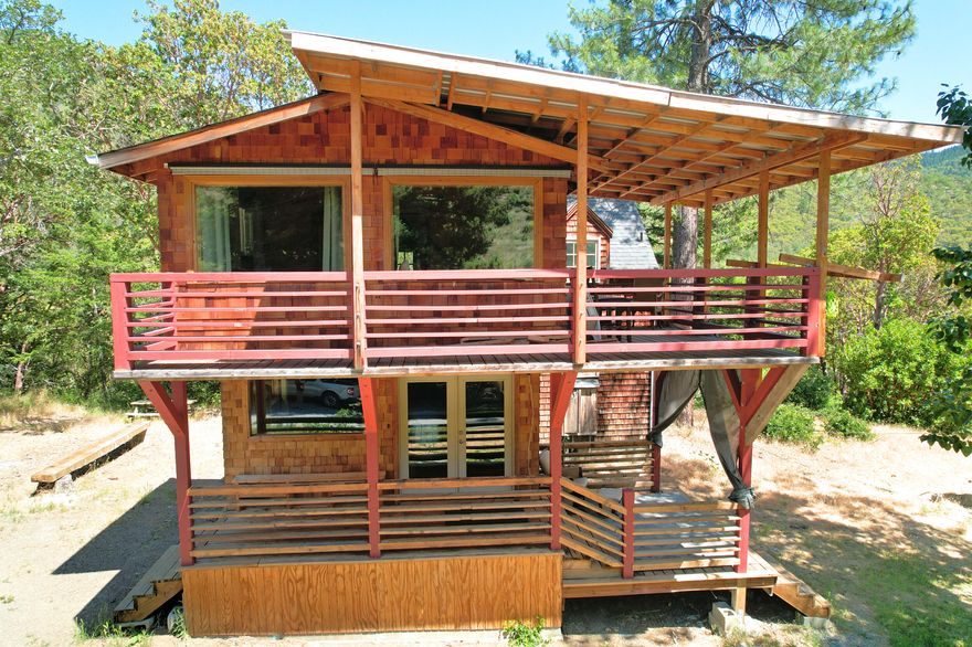 Charming Mini-Farm on Humbug Creek in the Applegate Valley. Cross a creek through the forest up to your own private little hobby farm homestead on 11.2 acres backed by 4,900 acres BLM. Unique, cozy custom built cedar sided home with dramatic architectural angles, custom details & rustic charm. Central wood stove, vaulted ceilings, stone & bamboo flooring throughout. Detached laundry room with additional storage & covered firewood area. Turn-key fenced & terraced garden area sports 3 automated greenhouses (one solar), mature fruit trees, blueberries, animal corrals & a chicken coop. Spacious workshop w/ vaulted ceiling is set up for wood stove, a previously certified kitchen & view into the attached hothouse. Hike up the hill to gorgeous views. A dreamy must see!