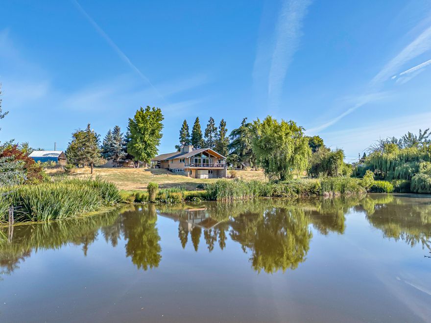 Extremely rare setting on a stunning year-round pond makes this a one-in-a-million property, truly unlike anything else. Lovingly owned by the seller for 43 years. Just minutes from town yet totally private, it features a gated entry, huge detached shop with concrete floors and power, large barn sits just behind the shop, flat usable grounds, high producing well (per seller), mature trees, and abundant wildlife. The home is fully vaulted with a floor-to-ceiling rock fireplace and natural light throughout. Main level has 2 bedrooms and a full bathroom. Downstairs includes a large 3rd bedroom, laundry area, and half bath. Includes city sewer and natural gas. Bright, open layout with tons of windows to enjoy the incredible views. Covered carport, full RV hookups, and just 4.3 miles to Fred Meyer. Ideal for animals or peaceful living. Rare opportunity with unmatched setting. Owner carry possible for qualified buyer.