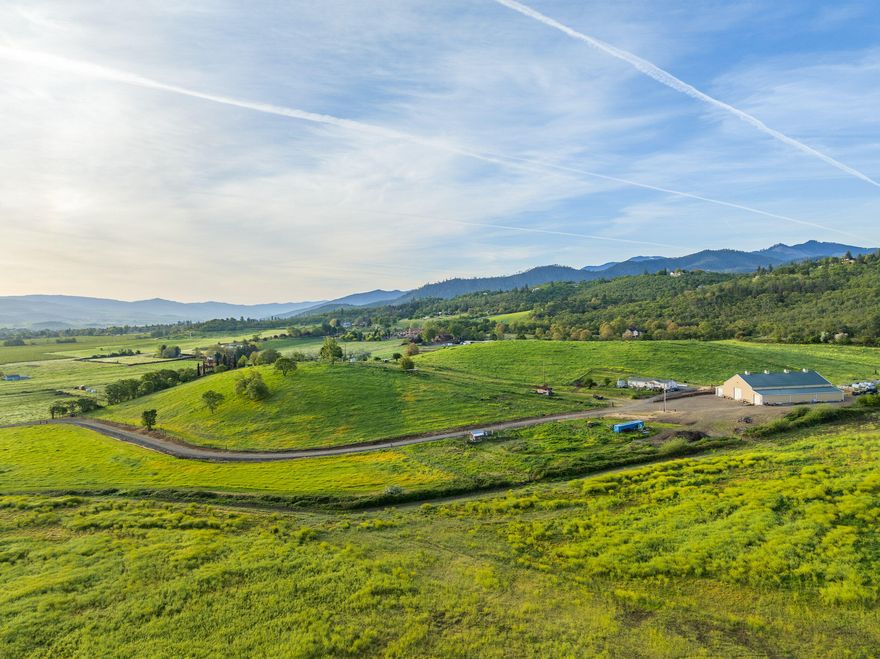 Located in the sought-after Southwest Medford foothills, Carpenter Hill Ranch offers 114 acres of gently rolling ground with panoramic views across the Rogue Valley—an exceptional setting for a future estate home. With 87.5 acres of irrigation rights and a mix of open pasture and vineyard, the property blends natural beauty with agricultural utility. Several premier building sites overlook the valley and mountains beyond, creating a rare opportunity for a signature residence in a serene rural setting. The 12-acre vineyard features a mix of varietals and includes 7 acres prepped for expansion. A 12,000 SF steel-framed shop (built 2002) includes a half bath and 200-amp power. The gravity-pressurized irrigation system includes risers, center pivot, and three bulges for water storage. Versatile soils support grazing, hay, or expanded vineyard. A well-kept 3-bed, 2-bath manufactured home serves as a ranch manager's residence while your vision takes shape.