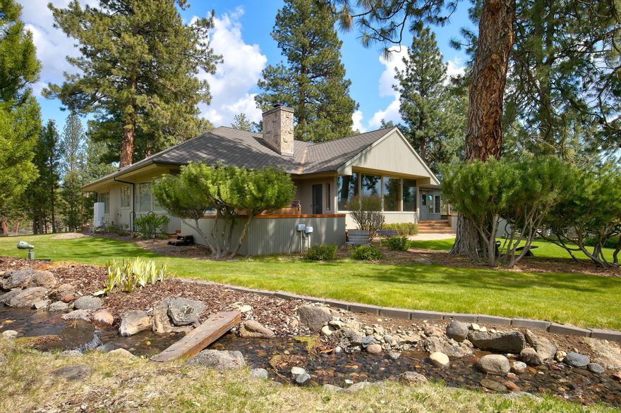 Discover your private retreat just minutes from downtown Sisters, boasting stunning views of the Three Sisters and Black Butte. This picturesque property, set on beautifully landscaped acreage, features a tranquil water feature with a waterfall and stream, perfect for serene living. The single-level home showcases a bright, open-concept layout. The spacious, updated kitchen effortlessly connects to the dining area and great room, highlighted by vaulted ceilings and a cozy wood-burning fireplace ideal for gatherings. This residence includes three bedrooms and three baths, featuring a luxurious primary suite with an ensuite bath, walk-in closet, and direct access to a deck overlooking the scenic grounds. Additional spaces include an office, laundry room, pantry, and a charming breakfast nook, thoughtfully designed for comfort. For hobbyists and outdoor enthusiasts, the home offers an oversized two-car garage and a 1,728 sq ft barn/shop, presenting endless possibilities.