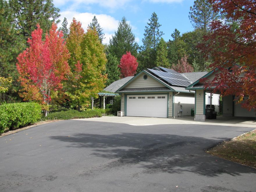 Close to town and a world away. Cute and clean single story (solar) home on a partially wooded parklike acre and tranquil screened in back porch area with quality decking.  Attached 2 car garage PLUS a detached extra-long two car garage/shop with additional extended covered carport area, all fully finished out. Open floor plan connects the kitchen, living and dining area. Spacious primary bedroom and bath, 3rd bedroom/office has a built in Murphy bed. 
The grounds are spectacular with decking area off of the screened in patio, high quality deer fenced gardening area and chicken coop, additional shed and much more.