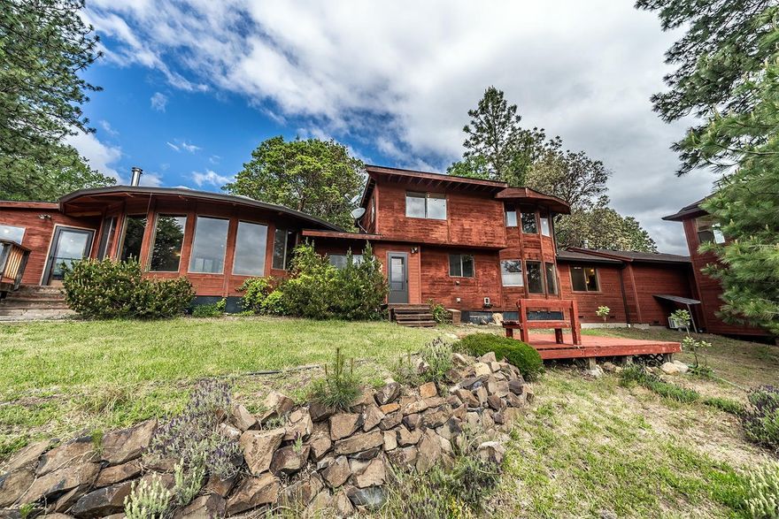 Charming one-of-a-kind custom home on private irrigated acreage within a mile of Emigrant Lake, and only 15 minutes from downtown Ashland's cultural amenities. Outstanding features include spacious light-filled circular rooms with exposed timber trusses, refinished madrone and oak hardwood flooring, solid core doors, and vessel sinks. The expansive master suite addition is outfitted with a large rock fireplace, floor-to-ceiling windows, multiple closets, ensuite bath with travertine tile, private deck, and meditation tower with views of Emigrant Lake. The kitchen is equipped with stainless appliances, gas range, granite counters, oak cabinetry, breakfast nook, and outdoor deck access. Recent updates to the home include geothermal heat pump and air conditioning, new water filtration system, refinished floors, interior and exterior paint, and new roofing. The property also has a 200 gpm artesian well, sizeable detached garage, storage shed, lush gardens, lawns, and acres of oak savanna.