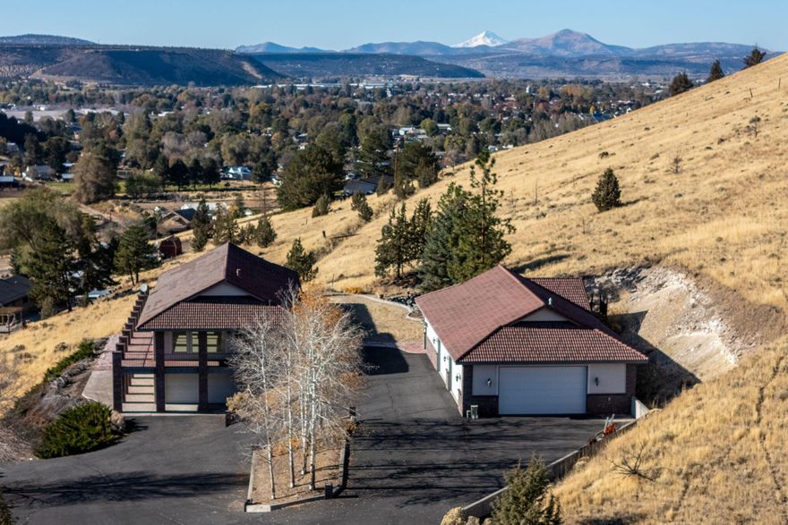 Majestic custom home on a total of 6.67 acres sited on a hillside with panoramic views of Juniper Canyon, Prineville and distant Mt. Jefferson. Grade level entrances on both upper and lower levels. Upper level with 4 beds, 2 full baths, main suite & ensuite, dining room, living room, huge family room, kitchen, etc. Lower level with 2 beds, full bath, kitchen, two living areas, and 2-car garage---potential for multi-generational living. Watch the sun rise and set from the wrap around deck and enjoy the large sunny patio. Spacious lawn and private setting with spectacular water feature for outdoor living. The impressive shop is 2880 sf with an upper level bonus room, high security 11'x11' vault, roughed in bath/laundry and A/C throughout. Extra large garage doors to fit all sizes of vehicles. Dedicated RV storage with power hookup. Lots of parking with large paved driveway...bring your toys!