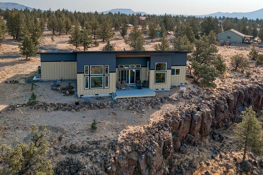 This sleek 1640 SF contemporary home on 6.19 acres offers breathtaking mountain views. It features 3 bedrooms, 2 baths, and a luxurious primary suite. The oversized 3-car garage and walls of windows provide stunning vistas. The kitchen includes custom cabinets, a large island with quartz counters, stainless steel appliances, and a pantry. A wall of glass showcases views of 8 mountain peaks, creating a seamless indoor-outdoor connection and passive solar heating. Outdoor living is enhanced by two decks and a large covered front patio. Drought-resistant landscaping includes a drip system and three water hydrants. The property is gated with outdoor gas hookups, and attic and crawl space lighting and outlets. Built in 2019, it has a high-end standing seam metal roof and many upgrades. Private well and standard septic included. Crooked River Ranch amenities: golf, pool, disc golf, dog park, pickleball, horse arena, and trails. Owner is a licensed broker in Oregon.