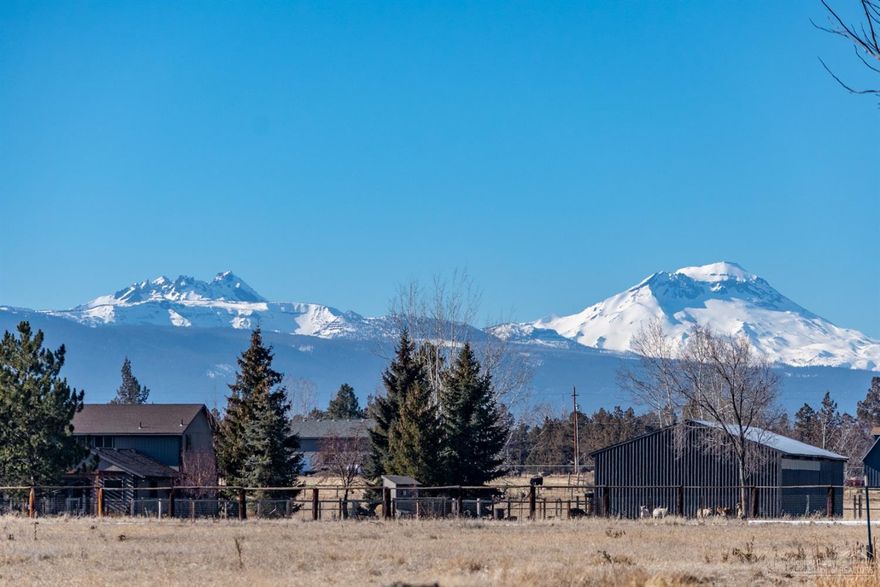 Panoramic Cascade Mountain views will capture your attention on these 5 peaceful acres in the heart of Tumalo. Perfectly situated for privacy and views. The home has been beautifully transformed by an artisan with custom woodwork, lighting, decks and pergolas, which beautifully complement the recently updated bathrooms, kitchen, and oversized bonus room. New windows, high efficiency heat pump water heater and propane fireplace add comfort and energy savings. New interior and exterior trim, paint and doors complete the makeover. Enjoy multiple outdoor living spaces to take in the Central Oregon sunshine and big views. With 4 acres of Swalley irrigation, the property is fenced and cross-fenced and setup for a hobby farm with outbuildings that include a 36x60 shop with 2-stall horse barn, separate goat barn and greenhouse. Located in a desirable Tumalo setting just 5 minutes to The Bite and Tumalo Coffeehouse and 10 minutes to shopping in Bend.