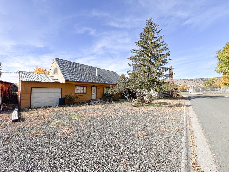 This 1950s home has undergone some remodeling.  It features vinyl windows and a tin roof. The flooring is a mix of laminate, wood, tile and carpet.

The homes heating is provided by a wood stove and an oil monitor stove. On the main level, there are two bedrooms, each with an armoire. The main level bathroom features a newly installed tub surround, vanity, and stylish tile flooring. There is also a finished bonus room, although it lacks a heat source. The upper level offers a 360-square-foot space that can serve as a primary bedroom. It includes a walk-in shower and an additional office area. 
The property includes an attached garage with a concrete floor, and there is a 13' x 11' storage area with a dirt floor. The outdoor space features a fenced back yard and a grape vine. The lot size is 0.17 acres and you can see the city park from your front yard.

This home is attractively priced for a quick sale, so do not hesitate to reach out for more information today!