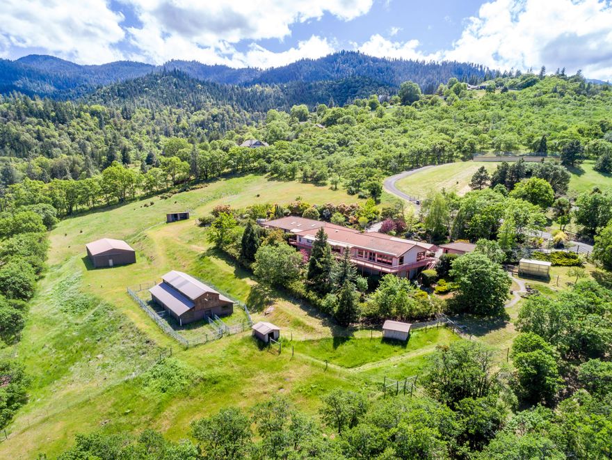 Rare single level view home on private acreage with two barns, just six minutes from groceries at Market of Choice. Patios and expansive decks with retractable awnings allow for year-round enjoyment of outdoor spaces. Quality features include solid oak flooring, hand-plastered interiors, vaulted exposed-beam ceilings, skylights, walls of windows, and multiple sets of French doors. Master suite has two spacious cedar-lined walk-in closets, sitting area with deck access, en-suite bath with shower, jetted tub, and ample counter space. Kitchen equipped with stainless appliances, display cabinets, pendant lighting, and island; adjacent great room with generous wet bar for entertaining. Additional amenities include an elegant library with custom shelving and fireplace, formal dining, sitting room, office, three guest bedrooms, en-suite bathrooms, laundry room, attached two-car garage, and a detached one-car garage. Mature gardens, fountain, greenhouses, raised beds, and security gates.