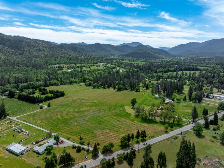 Amazing 81+ acre waterfront ranch in the heart of the Applegate Valley, offering exceptional versatility, income potential, and a premier location. This rare multi-family property includes 3 separate residences, each well-positioned for privacy and flexibility. With RR-5 zoning, the ranch carries significant development potential, creating incredible opportunities for expansion, family compound living, or long-term investment. The land is remarkably flat and usable, transitioning gently into beautiful sloped terrain, adjacent to BLM land. A historic barn, large shop, and extensive infrastructure improvements provide a powerful foundation for agricultural, livestock, or multi-use operations. The property boasts excellent irrigation water rights, a superb high-producing domestic well, and open pastures. Comprising four large parcels, the ranch is surrounded by gorgeous mountain views and offers unmatched tranquility while remaining close to everything—just 20 minutes to Grants Pass.