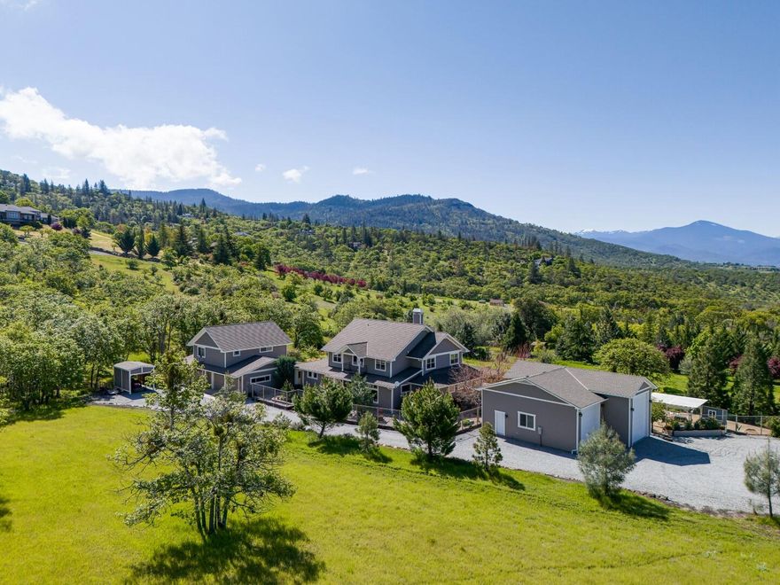 Located in the East Hills of Southern Oregon, this gated 5-acre property offers fantastic views of the surrounding mountains & valley. Cloaked in towering trees & lush mature gardens, the property echoes the serenity of a country retreat yet only minutes from town & RV Regional Medical Center. This contemporary farmhouse includes 2 primary suites, one on the main level w/a private entrance. Two additional 2nd level bedrooms, 2nd primary suite & a bonus area w/bath & living space above the oversized 4 car garage. Chef's kitchen w/granite countertops, professional grade appliances & Butler's pantry/wet bar w/wine refrigerator. Multiple living & dining spaces w/outstanding finish work. Expansive covered patio adorned w/charming wisteria overlooks a large pond w/waterfall & serene park-like grounds. Large pantry/mudroom, huge laundry room & exterior storage building. Workshop area, chicken coop, boat/RV storage garages, plus a tractor storage building. One of a Kind!
