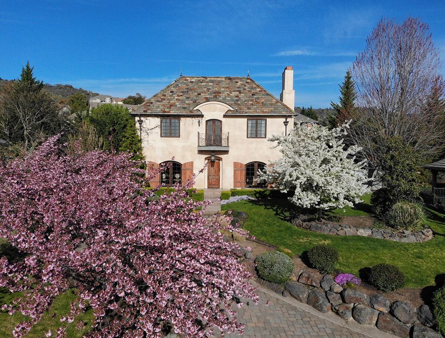 Old World French Eclectic styling with Chateau flavor originally constructed for the builder's personal residence!  Brick drive winds up to the home allowing for a knoll-top setting & sunset views.  Outside you'll discover period features like grapevine adorned stucco finish, slate roof, copper gutters & downspouts, hand-crafted wrought iron railings & gates, & a covered patio screened by a newly stucco'd wall flanking an outdoor fireplace.  Inside presents tile & hand-scraped hickory floors, hand-hewn exposed beams, plaster walls, 2 stone wood-burning fireplaces, lighted art alcove & more.  Spacious eat-in kitchen opens to a living area & features a 60-inch 6-burner Wolf Range with double ovens, chisel-edge granite counter, & butler's pantry to the formal dining room.  2nd living room off the front entry. French doors from expansive main-level master open to a private back courtyard.  Guest bedrooms are full suites, & there's a sizeable theater room with wet bar over the 3-car garage
