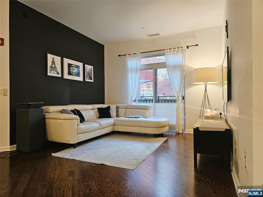 Discover effortless first-floor living at The M. This exceptional 2-bedroom +EXTRA den, 2.5-bath corner home offers approximately 1,410 sq ft of thoughtfully planned space with abundant natural light and easy access to the outdoors, making daily living comfortable and convenient. The residence features hardwood flooring throughout and a bright, open layout flowing seamlessly from the living area to a dedicated dining space and Juliet balcony. The contemporary kitchen offers a large island, granite countertops, tile backsplash, and stainless steel appliances. The primary bedroom suite provides a quiet retreat with a spacious walk-in closet and an en-suite bath with double vanity. The second bedroom includes a large closet and its own private bathroom, while the den offers flexible use as a home office, guest room, or additional living space. Additional conveniences include in-unit washer and dryer, one indoor parking space, and a new furnace and HVAC system for year-round comfort and efficiency. Residents enjoy access to community amenities including a pool, community room, and playground, all in a prime location near shops, restaurants, downtown conveniences, major highways, and easy NYC bus access. A rare low-maintenance opportunity with HOA covering gas, water, cable, and internet. First-floor living in one of the areaâ€™s most sought-after communities. Storage was additionally purchased by the owner.