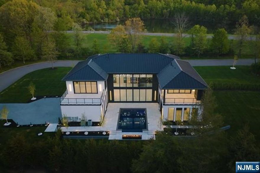 This architectural gem featuring 5 bedrooms, 7 full and 1 half bath radiates modern elegance. Its grand entrance showcases a stunning pivot door, revealing a light-filled foyer with towering windows. The two-story great room boasts panoramic views and flows into a state-of-the-art kitchen. A highlight of this home is a 3-story floating staircase crowned with a 28-foot chandelier. The property features a luxurious primary suite that offers unparalleled privacy, a spa-like bathroom, spacious walk-in, and a private balcony. The second floor features four additional luxe ensuite bedrooms. Outside is a custom pool backed by a fire pit lounge.