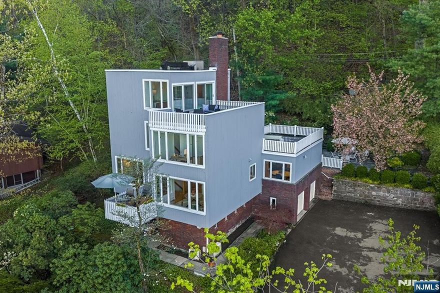 Perched high above Upper Montclair, this 5-bedroom, 3 1/2 bath, 1960 contemporary offers what may be the most extraordinary view of the New York City skyline in the entire region - visible from nearly every room, unobstructed, panoramic, and alive in every season. Surrounded by treetops, with the privacy and feeling of the Hollywood hills, it is a genuine sanctuary. At sunrise the skyline glows. At dusk it becomes a constellation of light. No neighboring roofline interrupts it. No future development threatens it. Inside, the home matches the view - warm, confident, and built to last. The expansive living room features a wall of windows framing the skyline and a wood-burning fireplace. A front deck and formal dining room share the same sweeping views. The kitchen, with its own eating area and adjoining family room - all with heated floors - create an easy rhythm for daily life and entertaining. The primary suite claims an entire floor of the home, offering a second wood-burning fireplace, wall of closets, en-suite bath with double vanity and walk-in shower, and its own private deck. In the rear, a large bluestone patio, gardens, and another large deck - quiet, private, and entirely your own. Laundry on the bedroom level. Beautiful hardwood floors. Recessed lighting. 3-zone heat. Top floor has central A/C; mini-splits cool the rest of the home. Whole-house generator, 2-car built-in garage, irrigation. 0.8 miles to Upper Montclair train. 12 miles to Midtown.