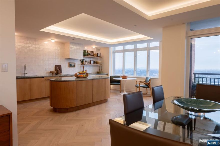 Perched at The Top, SOMA's premier luxury condominium, this fully renovated 3-bedroom residence showcases elevated design, exceptional craftsmanship, and sweeping NYC skyline views. Thoughtfully reimagined with a full designer renovation, every surface and finish has been curated with exceptional taste and attention to detail. An east-facing exposure fills the home with beautiful natural light throughout the day, enhanced by expansive windows and a seamless indoor-outdoor connection to a private balcony. New flooring laid in a sophisticated herringbone pattern, paired with sound-reducing underlayment, adds both style and comfort underfoot. Each of the three spacious bedrooms features its own ensuite full bath. The primary suite features a dressing area and bath with a soaking tub, stall shower w/new glass door, and refined new tile work. A stylish powder room off the hallway is ideal for guests, while custom built-in closets throughout provide exceptional storage solutions. The showstopping kitchen features custom wood cabinetry, marble counters, open shelving, and new appliances. A striking rounded center island anchors the space. Thoughtfully selected light fixtures and cove lighting on dimmers create the perfect ambiance throughout. Boasting one of the largest floorplans in The Top at 2500+ sqft, this home offers refined suburban living in the vibrant heart of Essex County, just moments from everything South Orange and Maplewood have to offer.