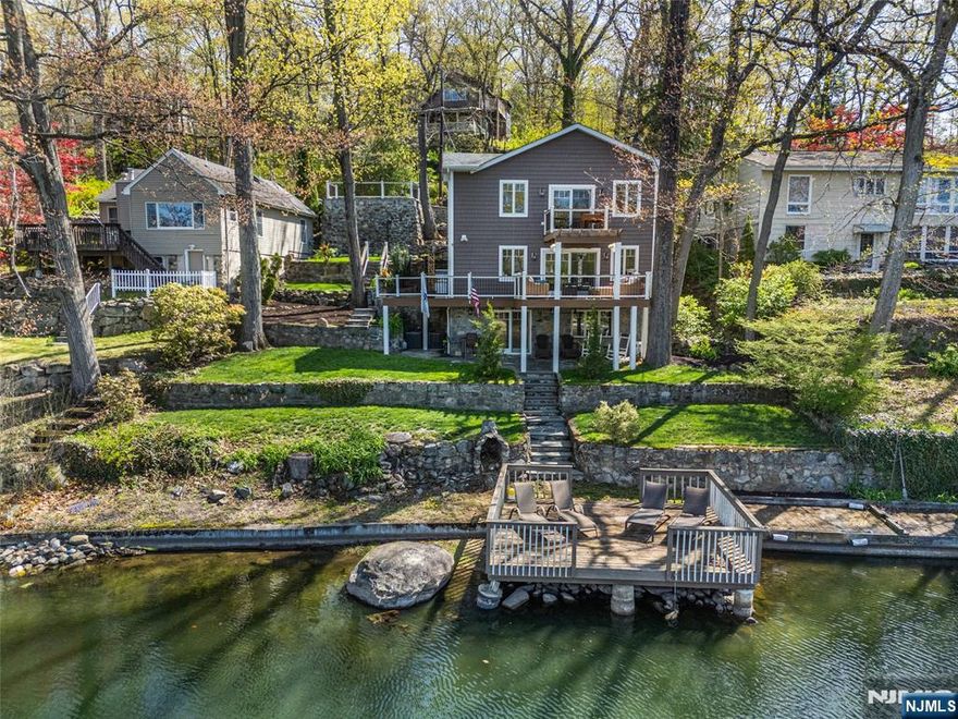 Completely rebuilt & expanded in 2021, this exceptional high-efficiency lakefront residence in Ringwood's coveted Erskine Lake community seamlessly blends modern luxury w-timeless lakefront design & an open-concept floor plan curated for effortless entertaining. The designer chef's kitchen showcases granite countertops, an expansive center island w-seating, high-end Samsung appliances & SS farmhouse sink, opening to the main living spaces. Rich hickory floors, striking wood-beam accents, exquisite interior stonework & walls of glass create a warm, sophisticated ambiance. The LR w-WB fireplace flows into an elegant leisure/sitting area w-sliders to a wraparound deck featuring a pergola, ceiling fan & lake views, plus natural gas grill hookup. Smart home enhancements include app-controlled lighting & door locks, professionally designed landscape lighting, masonry walls & custom stone steps. The primary suite offers a private BA & balcony overlooking the water. A 2nd and 3rd BR & renovated BA complete the upper level. The walkout LL "lake room" is designed for lakefront living & entertaining, featuring a half BA, waterproof finishes, seating, full-size refrigerator, custom built-ins & stonework, w-easy access from the lake. Glass sliders lead to a covered patio for indoor-outdoor living. A private dock invites boating, swimming & lakeside relaxation. Erskine Lakes offers a vibrant lifestyle w-beaches, clubhouse events & year-round activities. Floor plans avail.
