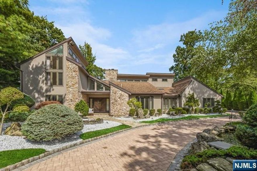 This distinctive contemporary home, set on a beautifully landscaped acre of privacy, is located on the prestigious East Hill of Cresskill. Built in the mid-80s, it offers over 7,500 sq. ft. of modern open living space. The grand, sun-filled entry foyer leads to a spacious family room, formal living and dining rooms, and a kitchen. The first floor features a large primary suite with a walk-in closet and luxurious bath, an office, guest bedroom with full bath, and a powder room. High ceilings and abundant natural light throughout. The second floor includes 3 bedrooms and 2 baths. The flat property boasts stunning waterfalls and ponds. The finished lower level offers 9' ceilings, a wet bar, full bath, bedroom, rec area, and storage. A 3-car garage completes this serene home. A must see!!!