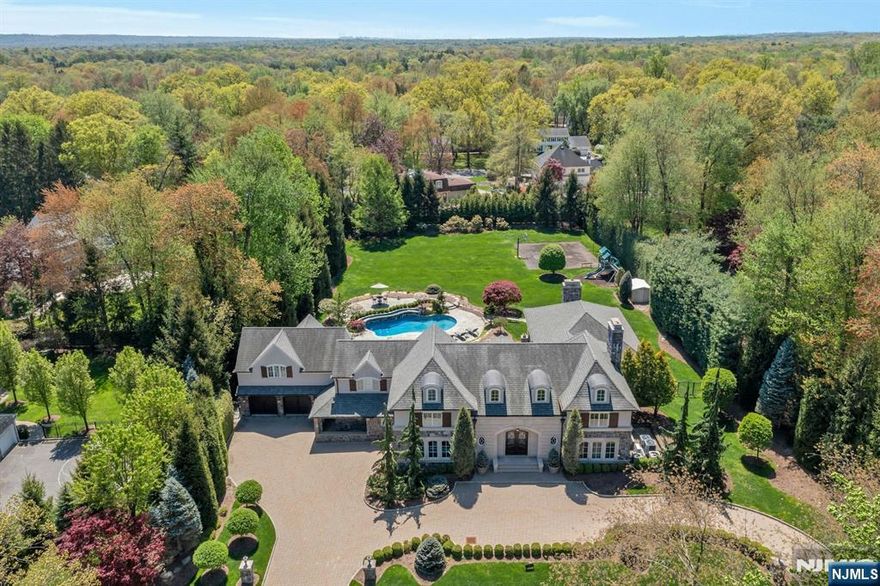 Experience luxury living in this exquisite estate featuring 5 ensuite bedrooms and 7 full baths across approx 6692 sqft of impeccably crafted space. With a stately stone and precast masonry facade, the home makes a striking first impression. A grand two-story foyer sets the tone with its elegant entry, leading to an intimate formal living room and a spacious formal dining room, perfect for refined entertaining. The large sun-drenched, south-facing gourmet kitchen showcases top-of-the-line appliances and opens to a grand great room with 20ft coffered ceilings and French doors leading to a sweeping loggia w/wood-burning fireplace. Nestled on 1.3 acres of resort-style grounds, the property boasts a gunite pool w/waterfall and direct access to a changing room and bath. Upstairs, the expansive primary suite offers a private balcony overlooking the pool, an oversized dressing room, and a spa-inspired bath. Adjacent is a vaulted-ceiling gym and a second luxurious bath w/soaking tub and shower. Three junior suites complete the upper level. A first-floor junior suite w/kitchenette offers ideal guest or multigenerational living or doubles as an in house cabana. The lower level features a playroom and pool room, perfect for fun and games. Blending timeless elegance with modern luxury, 21 Birchwood Rd is a rare opportunity to own an architectural masterpiece that offers exceptional comfort, refined design, and resort-style living in one of the area's most desirable settings.