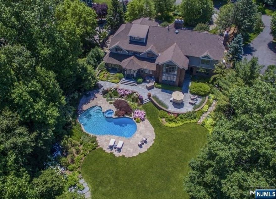 Live like you are on vacation every day in this modern North Caldwell estate, where bold design meets resort-style luxury. A dramatic marble entry and sweeping staircase set the tone, complemented by soaring ceilings, sleek millwork, and wide plank hardwood floors. Built with steel beam construction and surrounded by lush landscaping, water features, and curated gardens, the home offers exceptional privacy and tranquility. The Canterbury-style chefâ€™s kitchen anchors the main level with high-end appliances and timeless finishes, opening to a sun-filled glass solarium, perfect for year-round living. Upstairs, the primary suite delivers a true retreat with a spa bath, oversized shower, and soaking tub, while all additional bedrooms are spacious and ensuite.The finished lower level transforms the home into a private club, featuring a mahogany bar, climate-controlled wine cellar, FULL SWING GOLF PRO simulator, fitness room, projection theater, and lounge spaces designed for entertaining.