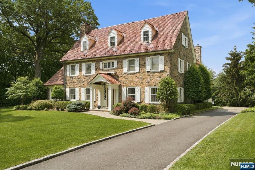 Situated on nearly an acre in Old Short Hills, this timeless fieldstone Colonial offers a rare balance of architectural significance and livability. From its classic facade to elegant proportions, the home invites you in with presence and warmth. Inside, a wide entry sets the tone. The living room, anchored by a wood-burning fireplace, flows into a sunroom with three stone walls and its own fireplace, offering a year-round connection to the outdoors. Light fills the formal dining room through multiple exposures, while a coffered ceiling adds refinement. A butler's pantry opens to a large kitchen designed for both form and function, with custom cabinetry, professional appliances and a breakfast room framed by stone and windows. French doors open to a bluestone patio and a backyard with room for a pool. A vaulted family room with exposed beams brings volume and ease, while a private office, mudroom and powder room complete the first floor. Upstairs, the primary suite offers a quiet escape with a spa-like bath and a custom walk-in closet. Three more bedrooms include two with en suite baths and one with an office. The third level continues with three bedrooms, two full baths and a lounge with versatility. The lower level includes a recreation room, gym, walk-in wine cellar and powder room, adding flexibility to any lifestyle. With a new cedar shake roof and a setting just blocks from town and the train, this is the rare home that pairs tradition with possibility inside and out.
