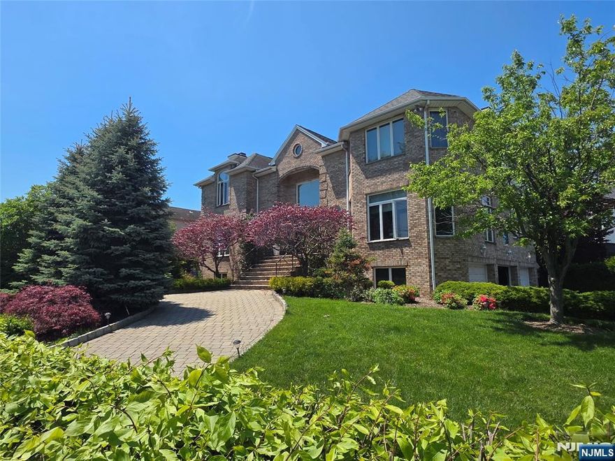 What luxury homes are for sale in Fort Lee, NJ, on the Bluff with NYC views? This one. Five-bedroom, four-and-a-half-bathroom center hall brick Colonial at 1115 Arcadian Way, Fort Lee, New Jersey 07024, in the Bluff section of Fort Lee, Bergen County. Corner lot, 11,286 square feet, with circular driveway and three-car attached garage. Built in 1997, renovated in 2011 with high-end contemporary finishes. Foyer features a limestone staircase, an ironwork railing, and Venetian plaster. First level: living room, formal dining room, family room with a fireplace, first-floor bedroom, powder room, laundry room, and a chef's Poggenpohl kitchen with Caesarstone counters, a Wolf six-burner gas range and double oven, and a Sub-Zero refrigerator. Second level: primary suite with fireplace and primary bath with soaking tub, second bedroom with ensuite bath, and two additional bedrooms with shared bath. Finished ground level offers a recreation room, a den, a full bath, tile flooring, and direct access to the three-car garage. Custom Wenge doors throughout, central vacuum, central air, two fireplaces, intercom, hardwood floors, professionally landscaped grounds. Partial Manhattan skyline and Hudson River views with east-facing exposure. Five minutes to the George Washington Bridge. NJ Transit Bus 158 and 159 to the Port Authority Bus Terminal board at Palisade Avenue and Bridle Way. Fort Lee Public Schools, Bergen County. 1115 Arcadian Way, Fort Lee, NJ 07024.