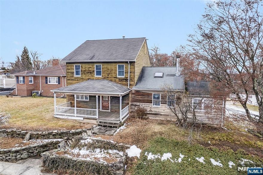 Positioned on nearly a half-acre in the heart of West Caldwell, this Colonial-style home stands out with its spacious layout, inviting front porch, and oversized two-car barn-style garage. The first floor opens into welcoming main-level living spaces, including a spacious living room and an expansive dining room with recessed lighting and a natural flow between the two areas. Filled with natural light, the eat-in kitchen features granite countertops, ample cabinetry, and direct access to the backyard. A first-floor bedroom and full bathroom offer flexible use for guests or a home office, while a separate laundry area adds everyday convenience. The second level offers two well-proportioned bedrooms, including a generously sized primary suite with a walk-in closet and an en-suite bathroom. The lower level provides substantial storage and utility space, offering flexibility and future potential. With some updating, this home offers the opportunity to reintroduce its character and elevate its full potential. Beyond the home, the property extends to a wooded backdrop that enhances privacy and is complemented by a rear porch. Conveniently located near West Caldwell's town center, parks, dining, and commuter routes, this home presents an opportunity to enjoy space, character, and potential within a desirable Essex County community. Central a/c is only on first floor.