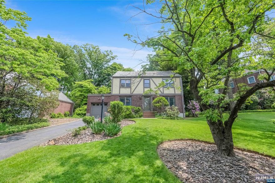 This Tudor style Center Hall Colonial is in move-in condition with plenty of upside potential. Set privately on an impressive 75 x 153 property with expansive sunset views. Approx. 2,418 sq ft (not including the basement or attached garage w/ EV charger) and offering four true levels of living space from the finished basement to the walk-up attic w/ a newly renovated bathroom in the junior ensuite. Pride of ownership is evident throughout this well appointed home featuring an updated eat-in-kitchen w/ granite counters, huge family room w/ vaulted ceiling & windows abound, sprawling living room w/ fireplace, elegant formal dining room, king sized primary suite, and generously sized spare bedrooms. Enjoy central air, a beautiful slate roof, 200 amp panel, ample closets & storage, and a professionally manicured property. Prime W. Englewood location near houses of worship, NYC transit, parks, shopping, and schools. Listed by Eric Wein (201-410-1556) of the Wein Agency (201-347-3044).