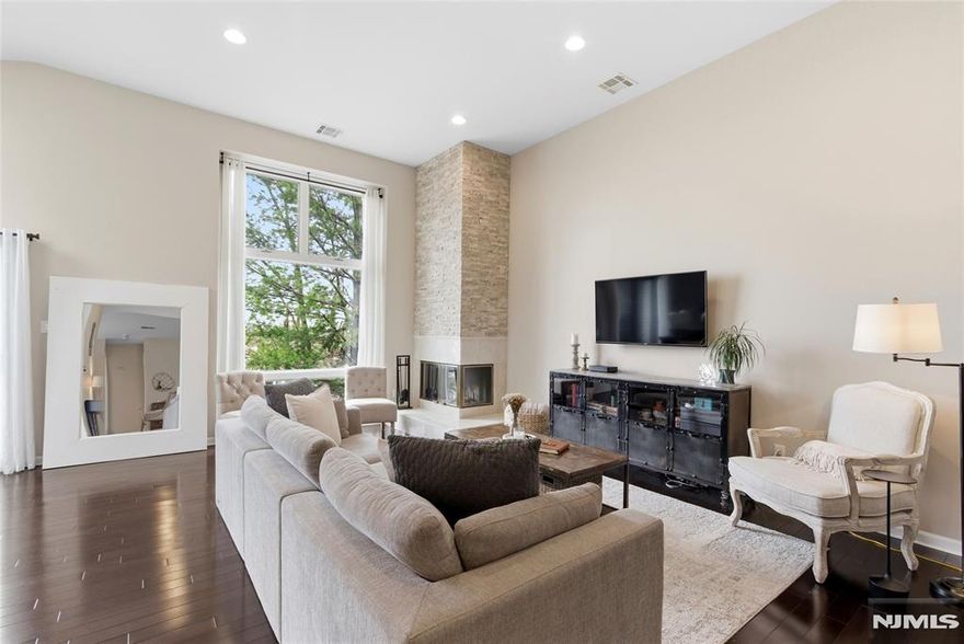 This end-unit townhome in Lyndhurst feels bright, open, and full of possibility from the moment you walk in. Soaring ceilings, skylights, and natural light from multiple exposures create an airy, uplifting feel, while the layout offers space that is easy to settle into and make your own. The main living area is expansive and welcoming, centered around a wood-burning fireplace that brings warmth and character. It is easy to picture cozy nights in, slow Sundays at home, or having friends over with city views as your backdrop. Just off the dining area, a private balcony creates a natural extension of the living space and a perfect spot for morning coffee, fresh air, or dinner outside. The den adds flexibility for a home office, reading room, workout space, or bonus hangout area, and it has its own balcony too. The bedroom offers private outdoor access as well. Each space feels generously sized, comfortable, and designed for real everyday living. With approximately 1,563 square feet, two bedrooms, two full baths, and room to spread out, this home offers a strong balance of function and charm. Central air, a one-car garage, and an additional outdoor parking space add convenience, while the location near Route 3, the NJ Turnpike, NJ Transit, shopping, dining, and local recreation makes everyday life that much easier.